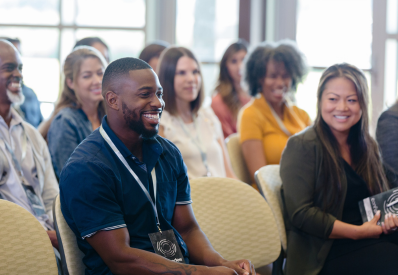 Conference audience members, a black man and asian women are smiling.